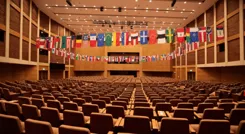 Un grand auditorium rempli de drapeaux et de bannières colorés, symbolisant diverses cultures éducatives, des chaises vides disposées pour les participants, témoignant d'une atmosphère d'anticipation et de collaboration mondiale.